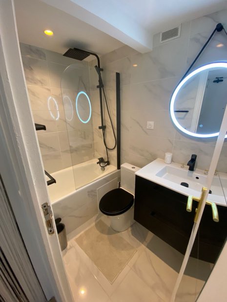 Salle de bains rénovée : baignoire, colonne de douche noire, meuble vasque et WC